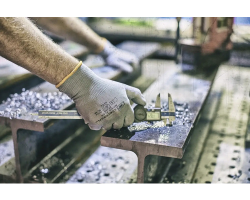 En person mäter en metallbit med ett digitalt skjutmått på en balk.