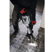 En man med arbetshandskar använder en bilningshammare för att ta bort plattor.