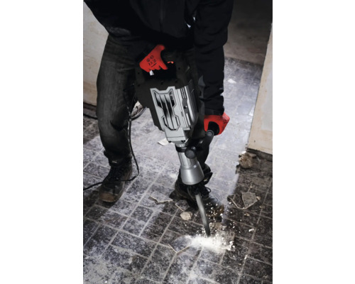 En man med arbetshandskar använder en bilningshammare för att ta bort plattor.