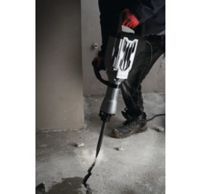 En man använder en bilningshammare för att skapa en spricka i ett betonggolv.