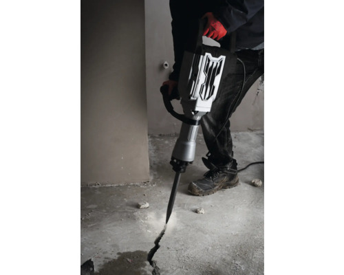 En man använder en bilningshammare för att skapa en spricka i ett betonggolv.