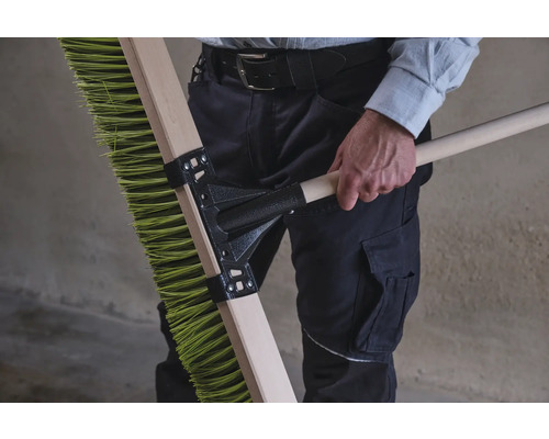 Person håller en grön sopborste med träskaft.