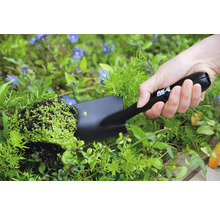 Person håller en handspatel med växt i trädgården.