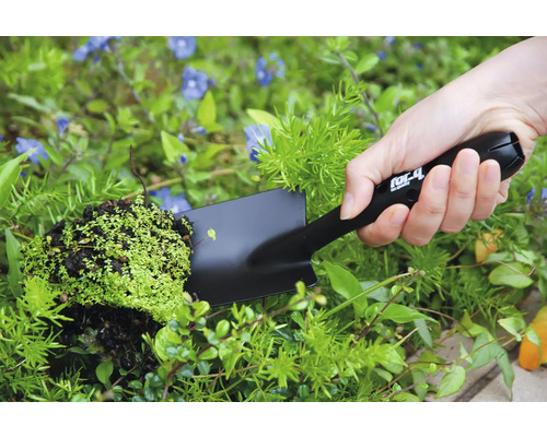 Person håller en handspatel med växt i trädgården.