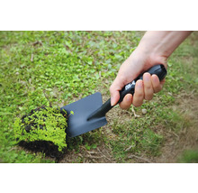 En person håller en svart trädgårdsspade med en bit jord och växter.