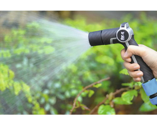 En hand håller en trädgårdsspruta och vattnar växter.