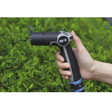 Trädgårdsspruta i handen framför buskar