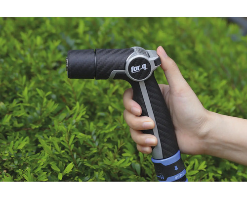 Trädgårdsspruta i handen framför buskar