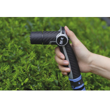 En hand håller en trädgårdsspruta av märket For Q framför en grön buske