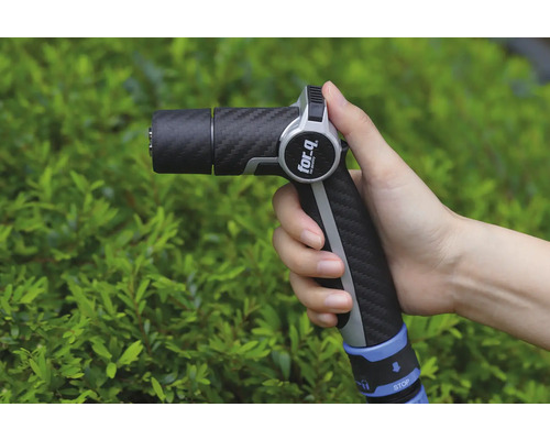 En hand håller en trädgårdsspruta av märket For Q framför en grön buske