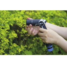 En person håller en trädgårdsspruta från for_q framför en grön buske.