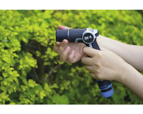 En person håller en trädgårdsspruta från for_q framför en grön buske.