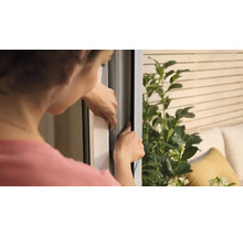 Kvinna fäster ett insektsnät på ett fönster.