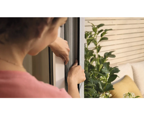 Kvinna fäster ett insektsnät på ett fönster.
