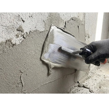 En person slätar ut gips med en spackelspade på en vägg.