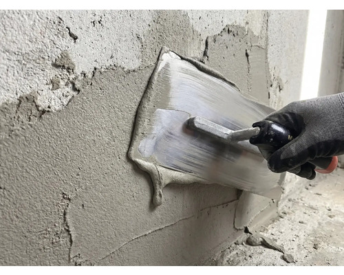 En person slätar ut gips med en spackelspade på en vägg.