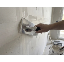 Hantverkare jämnar väggen med spackel och puts