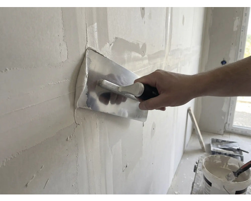 Hantverkare jämnar väggen med spackel och puts