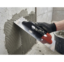 Applicera kakelfix på en vägg med en spatel i rostfritt stål