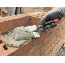 En murare applicerar murbruk på en tegelvägg med en murslev.