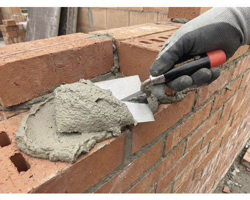 En murare applicerar murbruk på en tegelvägg med en murslev.