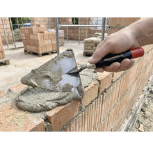 Murare lägger tegelstenar med en murslev och murbruk.