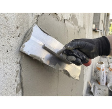 Hantverkare jämnar ut puts med en murslev på en vägg.