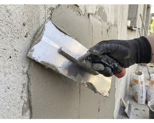 Hantverkare jämnar ut puts med en murslev på en vägg.