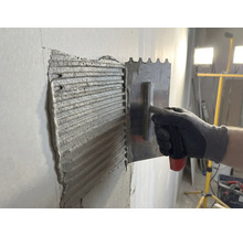 Kakellim appliceras på en vägg med en spatel i rostfritt stål