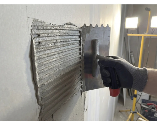 Kakellim appliceras på en vägg med en spatel i rostfritt stål