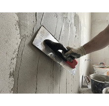 Hantverkare applicerar puts på en vägg med en murslev.