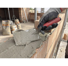 Murare arbetar med en murslev på en tegelvägg, cementsäckar i bakgrunden.