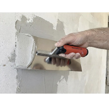 En person jämnar ut gips med en putsbräda på en vägg.