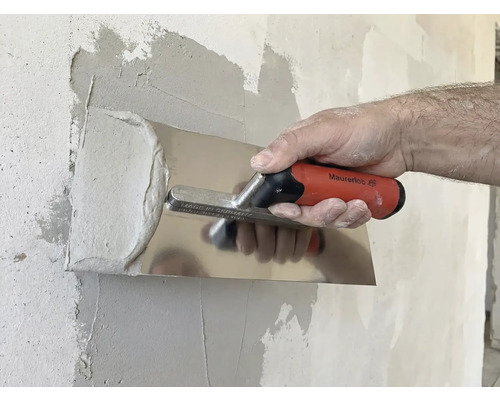 En person jämnar ut gips med en putsbräda på en vägg.