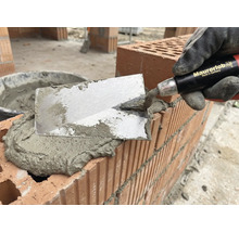 Murare med murslev applicerar murbruk på tegelstenar för murverk