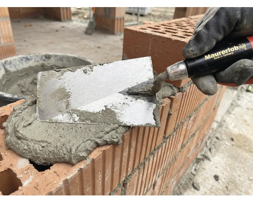 Murare med murslev applicerar murbruk på tegelstenar för murverk