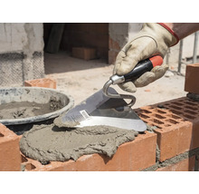 Murarhand med murslev som applicerar murbruk på tegelstenar