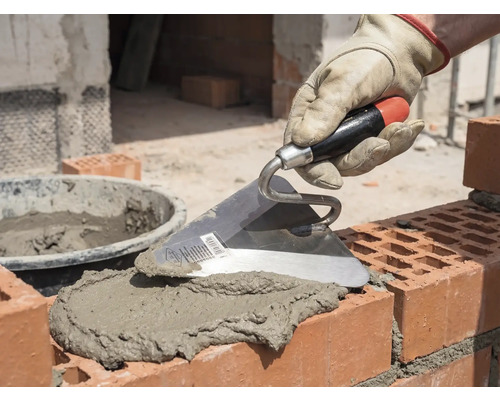 Murarhand med murslev som applicerar murbruk på tegelstenar