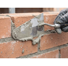 Murare som fogar en tegelvägg med en murslev