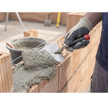 Murare som applicerar murbruk och tegelstenar för att bygga en vägg