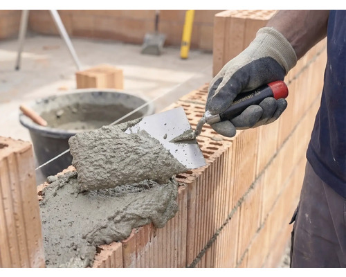 Murare som applicerar murbruk och tegelstenar för att bygga en vägg