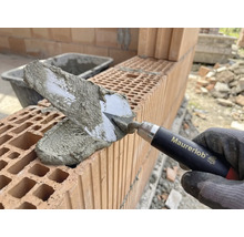 Murarens hand med murslev applicerar murbruk på tegelstenar