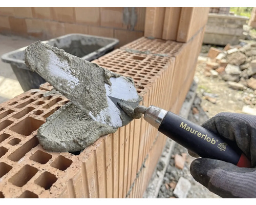 Murarens hand med murslev applicerar murbruk på tegelstenar