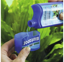 JBL Biotopol vattenberedningsmedel hälls i doseringsmåttet med akvarieväxter i bakgrunden.