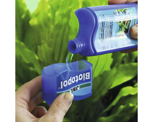 JBL Biotopol vattenberedningsmedel hälls i doseringsmåttet med akvarieväxter i bakgrunden.