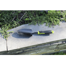 Trädgårdsspade på en mur med växter i bakgrunden