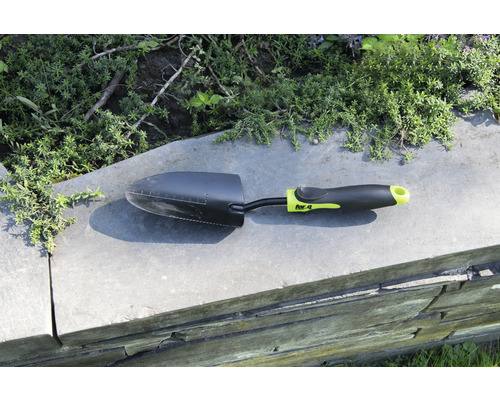 Trädgårdsspade på en mur med växter i bakgrunden