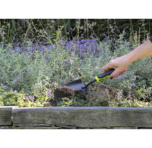 En person använder en liten trädgårdsspade för att gräva i en blomsterrabatt.