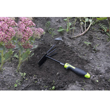 Trädgårdsredskap med kratta och hacka i rabatten bredvid en växt