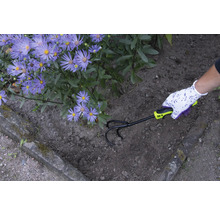 Trädgårdsmästare luckrar upp jorden med en kultivator bredvid lila blommor.